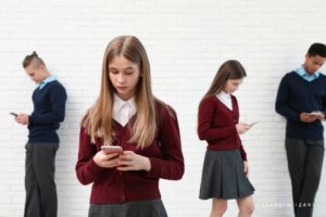 Grupo de adolescentes con uniforme mirando el móvil sin interactuar entre ellos, simbolizando el impacto de las pantallas en la autoestima