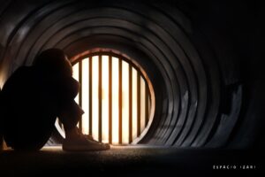 Persona sentada sola en un túnel oscuro frente a una reja iluminada, simbolizando la ansiedad silenciosa y sus síntomas invisibles